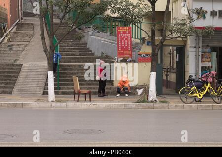 Kunming, Yunnan, Chine - 30 décembre 2017 : deux femmes chinoises sur le trottoir avec une chaise Banque D'Images