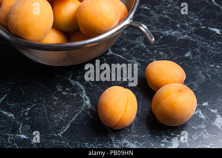 Organique mûres les abricots dans une passoire en acier. Composition dans un style rustique - jaune bio abricots juteux dans son ensemble et passoire en acier et des moitiés d'abricots o Banque D'Images