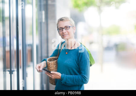Femme debout à l'extérieur d'un supermarché tenant son téléphone mobile et une carte de crédit Banque D'Images