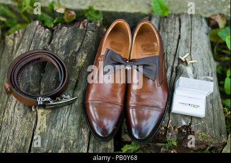 Photo en gros plan des chaussures du marié, boutons de manchette, ceinture et noeud papillon sur la surface en bois. Banque D'Images