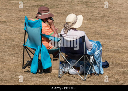 Deux dames plus âgées assis dans des chaises sur un terrain desséché pendant la vague sur une chaude journée d'été porter un chapeau. Banque D'Images