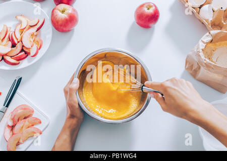 Processus de cuisson de la tarte aux pommes, vue du dessus. Woman's hands fouetter les œufs et le sucre dans un bol pour faire de la pâte. Banque D'Images
