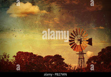 Moulin rustique entourée d'arbres sur les terres agricoles sous un ciel lever du soleil dans les régions rurales de NSW, Australie. Image texture grunge avec copie espace pour le texte. Banque D'Images