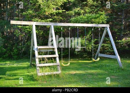 Swingset en bois abandonnée en face de la forêt avec un peu de végétation d'herbe sur une journée ensoleillée en été, Prince Edward Island, Canada Banque D'Images