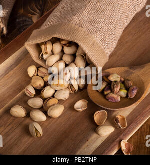 Pistaches déversés par un sac de toile et une cuillerée de noix sur une planche en bois Banque D'Images