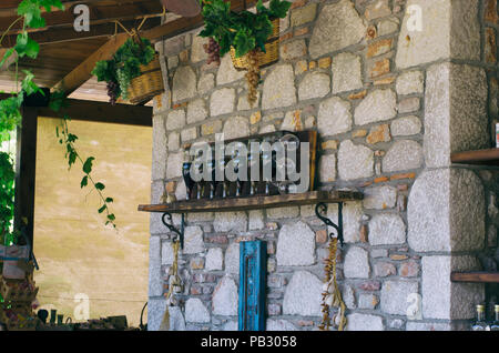 Les bouteilles de vin et des verres sur un plateau fixé sur un mur en pierre décorée avec des paniers de raisins Banque D'Images