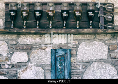 Les bouteilles de vin dans une rangée avec des verres sur un plateau en bois contre un mur de pierre avec stylisation sous un film Banque D'Images