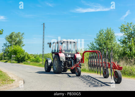 Tracteur avec faneuse on rural road sur sunny day Banque D'Images