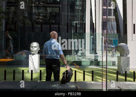 Un bureau à tête travailleur attend à côté de la tête sculptures intitulées Numen (passage fête votive Un et Deux) par Thomas J Prix à l'extérieur le Leadenhall Building pendant la canicule de 2018 dans la ville de Londres, le quartier financier de la capitale, le 24 juillet 2018, à Londres, en Angleterre. Banque D'Images