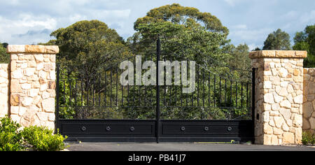 Metal entrée portes d'entrée de la propriété rurale mis en grès brique clôture avec l'eucalyptus gum arbres en arrière-plan Banque D'Images