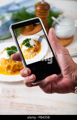 L'homme prend une photo de l'alimentation sur le téléphone. Choux paresseux sur une table en bois. Délicieux dîner fait maison. Banque D'Images