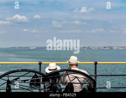 Jeune couple assis sur un banc, ovelooking la mer portant des chapeaux de paille. Banque D'Images