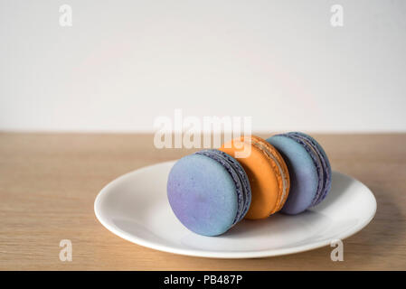 Trois Macarons Orange et bleu assis sur leurs côtés sur une plaque Banque D'Images