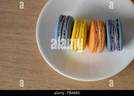 Quatre Macarons debout sur leurs côtés sur une plaque blanche sur une table en bois Banque D'Images