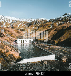 Piscine naturelle en Islande Seljavallalaug avec l'homme dans l'eau et temps de neige et les montagnes tout autour. Beau temps et ciel bleu. Banque D'Images