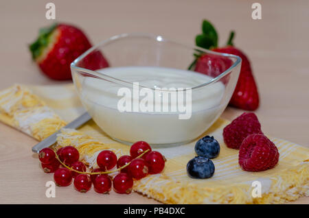 Framboises, bleuets, fraises et des mûres avec du yogourt dans un bol en verre sur une serviette jaune sur une table en bois Banque D'Images