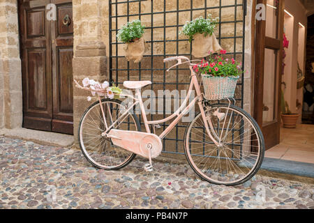 Painted Ladies rose vélo avec des fleurs en rue avec des portes anciennes et des pierres sur l'île de la Sardaigne Banque D'Images