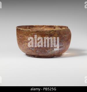 Bol en verre. Culture : Roman. Dimensions : Hauteur : 2 in. (5,1 cm) Diam. : 3 7/8 x 2 5/8 in. (9,8 x 6,7 cm). Date : 2ème-3ème siècle de notre ère. Incolore à bleu pâle, teinte verte, Vertical, arrondi et épais rebord ; côtés verticaux à corps, puis en courbe à l'anneau de base appliquée ; légèrement inégale, base plate avec pontil centrale scar et coup de pied sur l'intérieur. Cassé et réparé, part de RIM et côté supérieur manquant, et un trou dans la partie inférieure du corps ; et en soufflant des bulles piqûre piqûres ; stries, ternissement, et l'altération irisé couvrant toute la surface. Musée : Metropolitan Museum of Art, New York, USA. Banque D'Images