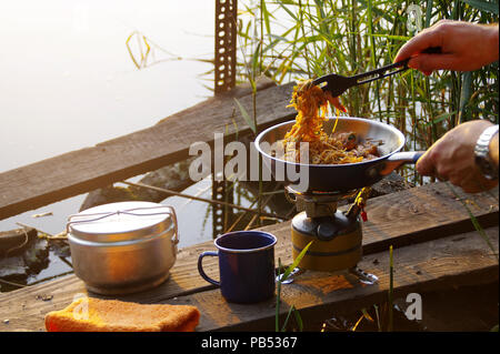 Camping de l'alimentation. Des pâtes sur le moule sur feu touristiques cuisinière. La cuisine du Camp sur la rive du lac. Banque D'Images
