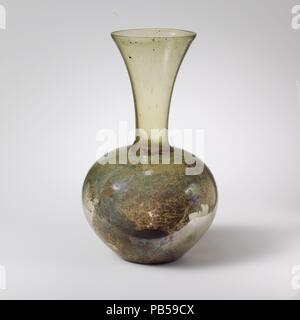 Bouteille en verre. Culture : Roman. Dimensions : 7 1/4''. (18.4cm). Date : 4ème siècle de notre ère. La lumière translucide vert. Jante légèrement inégale, fissurés et sol, en entonnoir ; cou large, globulaire, effilé vers le bas du corps ; fond concave. Décoré avec des bandes de frottement roue-lignes horizontales : l'un juste au-dessous de rim, quatre autres bandes sur le haut du corps. Intacts ; beaucoup de piqûre et quelques grosses bulles, et soufflant de stries, avec quelques inclusions noires au cou ; léger ternissement et iridescence sur l'extérieur, les grandes parcelles de terre l'incrustation, intempéries, et brillant sur l'iridescence de l'intérieur. Bottl Banque D'Images