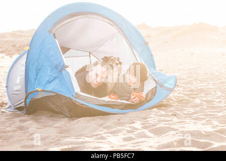 Couple le téléphone intelligent et avoir du plaisir à l'intérieur d'une tente dans un camping sur la plage chien border collie derrière eux regardant la caméra. Banque D'Images