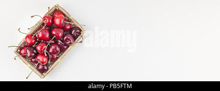 Longue et large bannière de cerise mûre fraîche dans un petit panier en osier avec copie espace isolé sur fond blanc un style minimaliste. Notion de plaisir d'été et guérir Banque D'Images