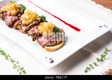 Rosbif aux oignons frits sur des morceaux de baguette on white plate Banque D'Images