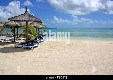 Des chaises longues et des parasols en chaume lors d'une merveilleuse plage de sable blanc et eau turquoise à l'Ile Maurice Banque D'Images