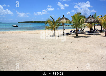 Des chaises longues et des parasols en chaume lors d'une belle plage de sable blanc à l'Ile Maurice - un bateau à l'ancre dans le lagon Banque D'Images