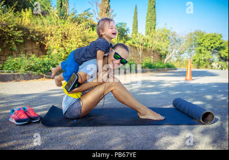 Une vie familiale saine, cute cheerful baby boy joue piggy back et l'aide à faire des étirements, belle femme avec son petit fils faire excercise sport Banque D'Images