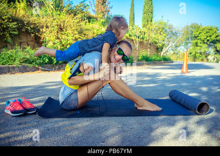 Une vie familiale saine, cute cheerful baby boy joue piggy back et l'aide à faire des étirements, belle femme avec son petit fils faire excercise sport Banque D'Images