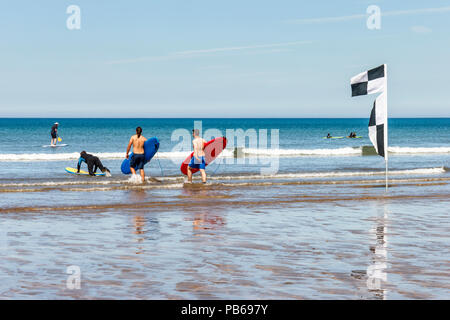 Surfers carrying leurs conseils à la mer sur une chaude journée à Westward Ho !, Devon, UK Banque D'Images