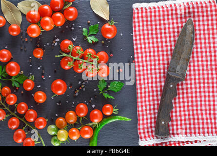 Tomates cerises rouges mûrs sur les rameaux assaisonnés de sel et de poivre et d'un couteau , fond noir graphite Banque D'Images
