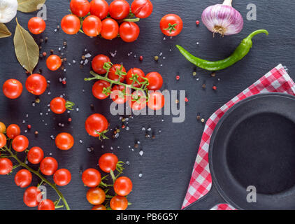 Frais mûrs tomates cerises rouges sur les branches sont assaisonnés de sel et de poivre, à côté du poêle rond noir vide, vue du dessus Banque D'Images