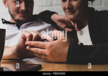 L'homme la main caresse une femme de main. Dans le contexte de l'homme heureux et la jeune fille sont visibles. Devant eux sur une table se trouve le téléphone. La phot Banque D'Images