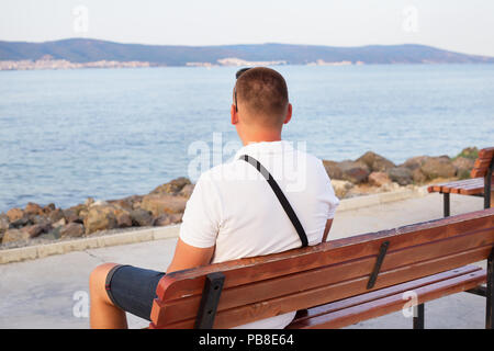 Le mec est assis sur un banc et regarde la mer Banque D'Images