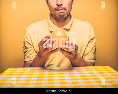 Un jeune homme assis à une table est excité à l'idée de manger un pamplemousse et peut à peine attendre Banque D'Images