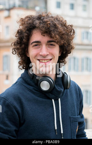 Portrait de beau jeune homme avec les cheveux bouclés avec des écouteurs autour de son cou Banque D'Images