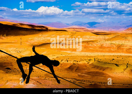 Silhouette d'athlète sautant à la perche avec dunes de sable orange et montagnes en désert du Sahara à l'arrière-plan Banque D'Images