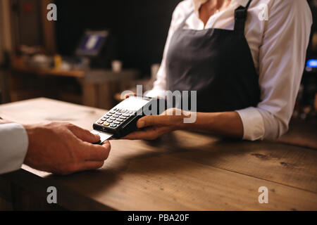 Female bartender holding un lecteur de carte de crédit avec la machine client mâle l'insertion de la carte dans la machine pour le paiement. Banque D'Images