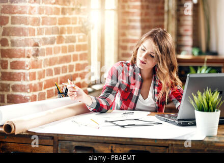 Jolie femelle ambitieux architecte en chemise à carreaux dimensions un nouveau projet en bureau loft Banque D'Images