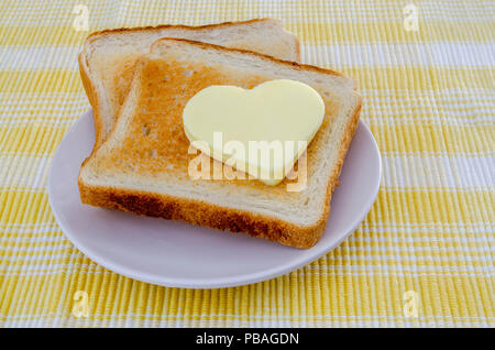 Deux toasts avec du beurre en forme de cœur sur une nappe jaune Banque D'Images