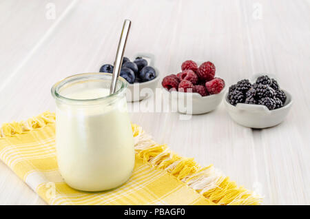 Le yogourt dans une tasse en verre avec des fruits rouges sur une serviette jaune sur une table en bois blanc Banque D'Images