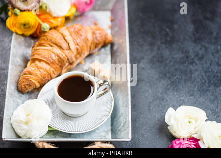 Petit-déjeuner léger de croissants frais et une tasse de café sur le bac gris, Ranunculus fleurs à proximité Banque D'Images