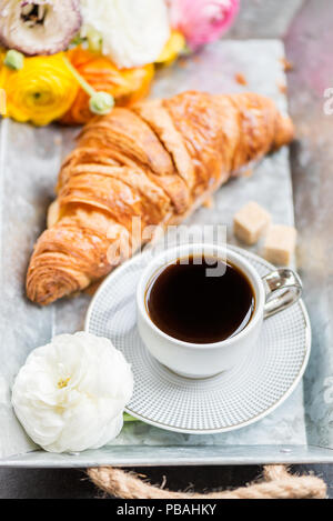 Petit-déjeuner léger de croissants frais et une tasse de café sur le bac gris, Ranunculus fleurs à proximité Banque D'Images