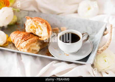 Petit-déjeuner au lit de croissants frais et une tasse de café sur le bac gris, Ranunculus fleurs à proximité Banque D'Images