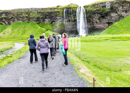 Seljalandsfoss, Islande - 14 juin 2018 : Cascade, falaise, Green Grass Hills, beaucoup de touristes, des gens qui marchent sur la saleté de gravier, de l'eau tomber de cli Banque D'Images