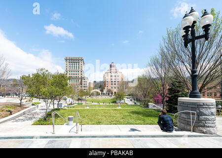 Asheville, États-Unis - 19 Avril 2018 : Retour du jeune homme assis millénaire hipster en regardant les bâtiments, le palais de justice et la Green Pack Square Park en hippie Aucun Banque D'Images