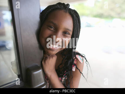 Dix ans African American girl sourit et ouvre la porte de l'école. Banque D'Images
