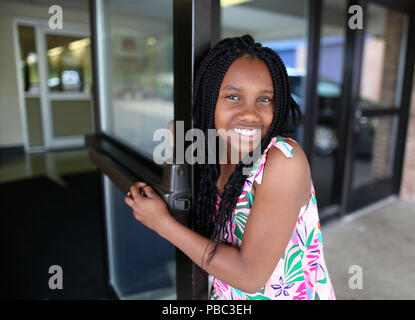Dix ans African American girl sourit et ouvre la porte de l'école. Banque D'Images